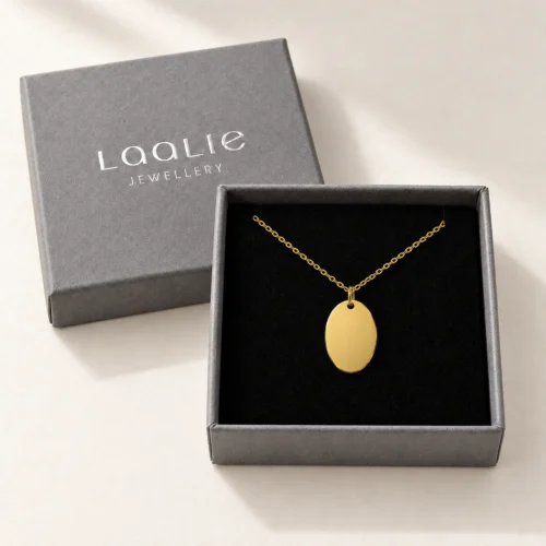 Plain 12 x 18mm gold coloured stainless steel oval necklace displayed in an open grey Laalie gift box.