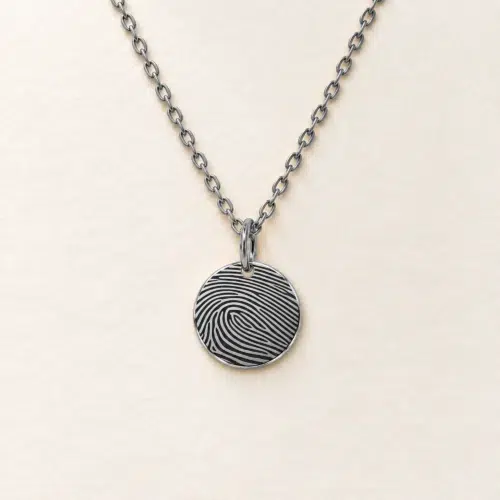13mm silver coloured stainless steel disc necklace with fingerprint engraving on an ivory background