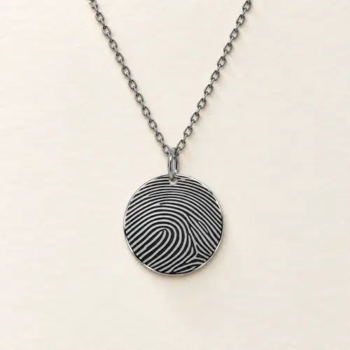 15mm silver coloured stainless steel disc necklace with fingerprint engraving on an ivory background