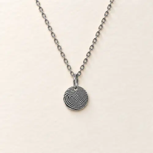 9mm silver coloured stainless steel disc necklace with fingerprint engraving on an ivory background