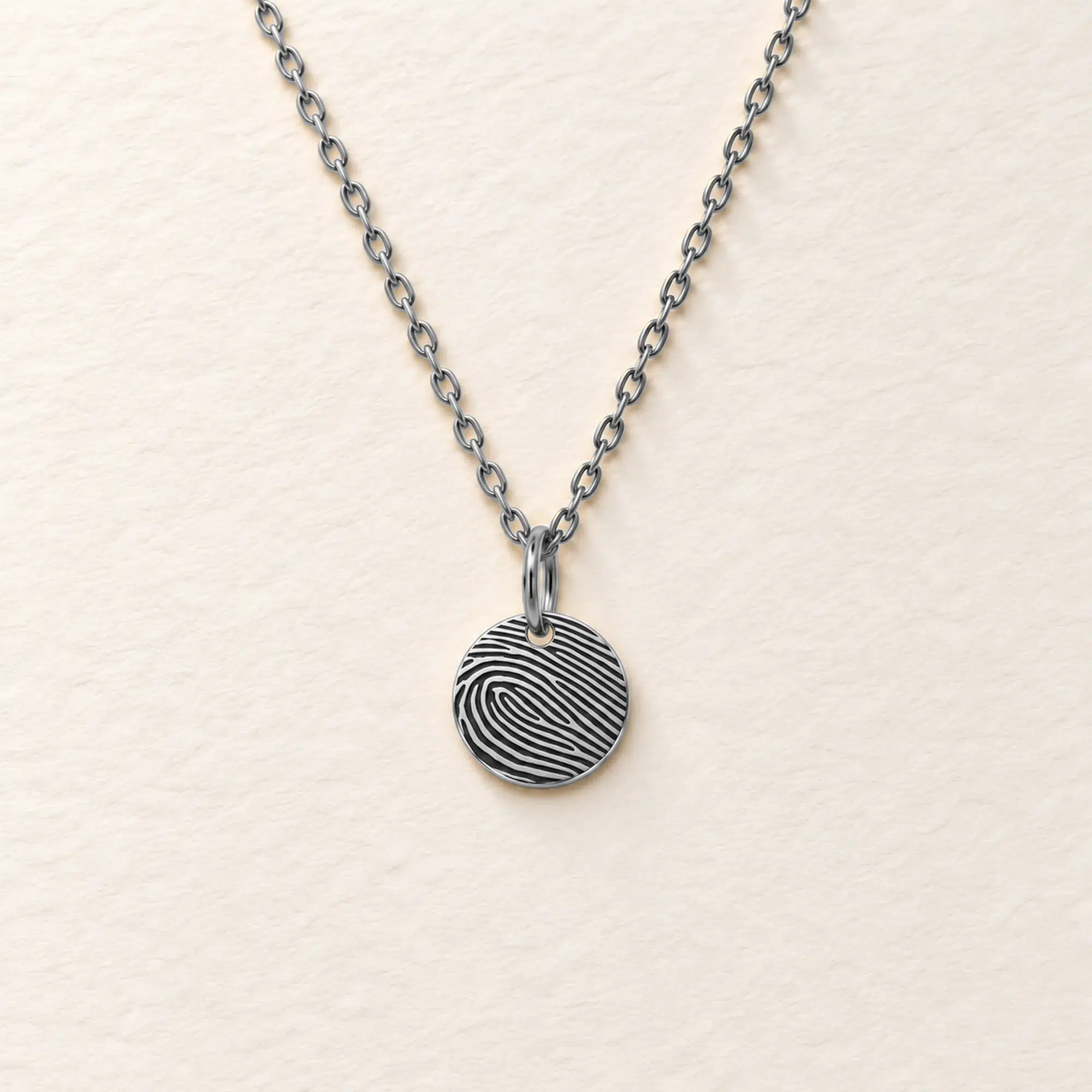 9mm silver coloured stainless steel disc necklace with fingerprint engraving on an ivory background