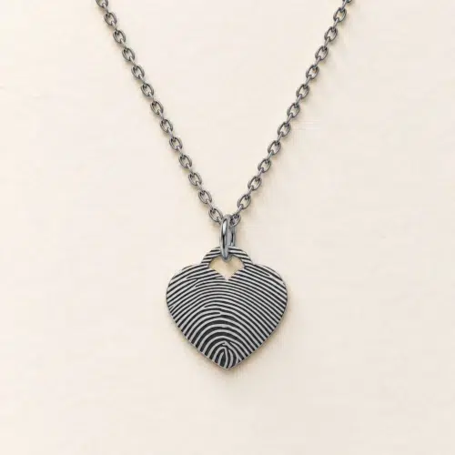 15mm silver coloured stainless steel heart necklace with fingerprint engraving on an ivory background