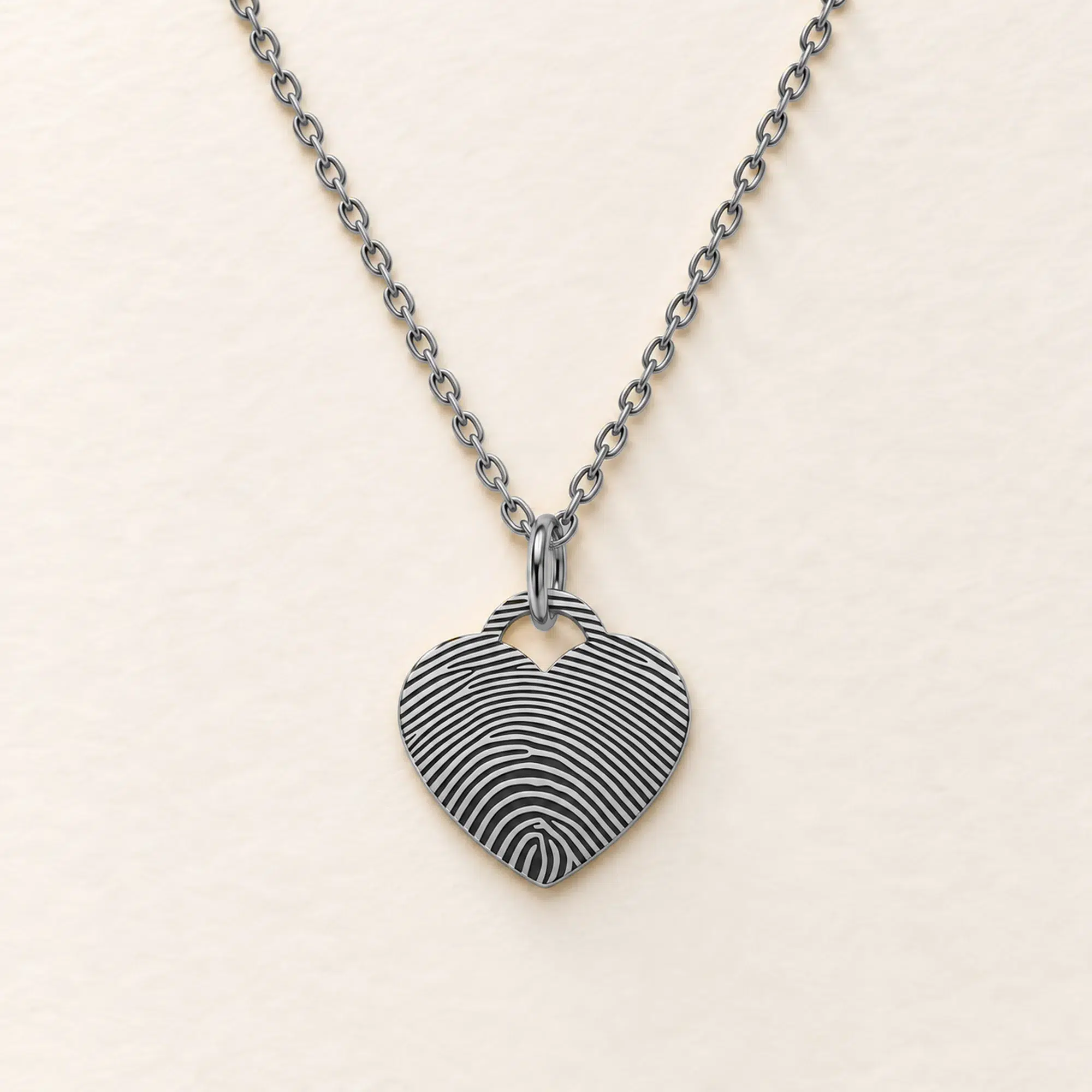 15mm silver coloured stainless steel heart necklace with fingerprint engraving on an ivory background